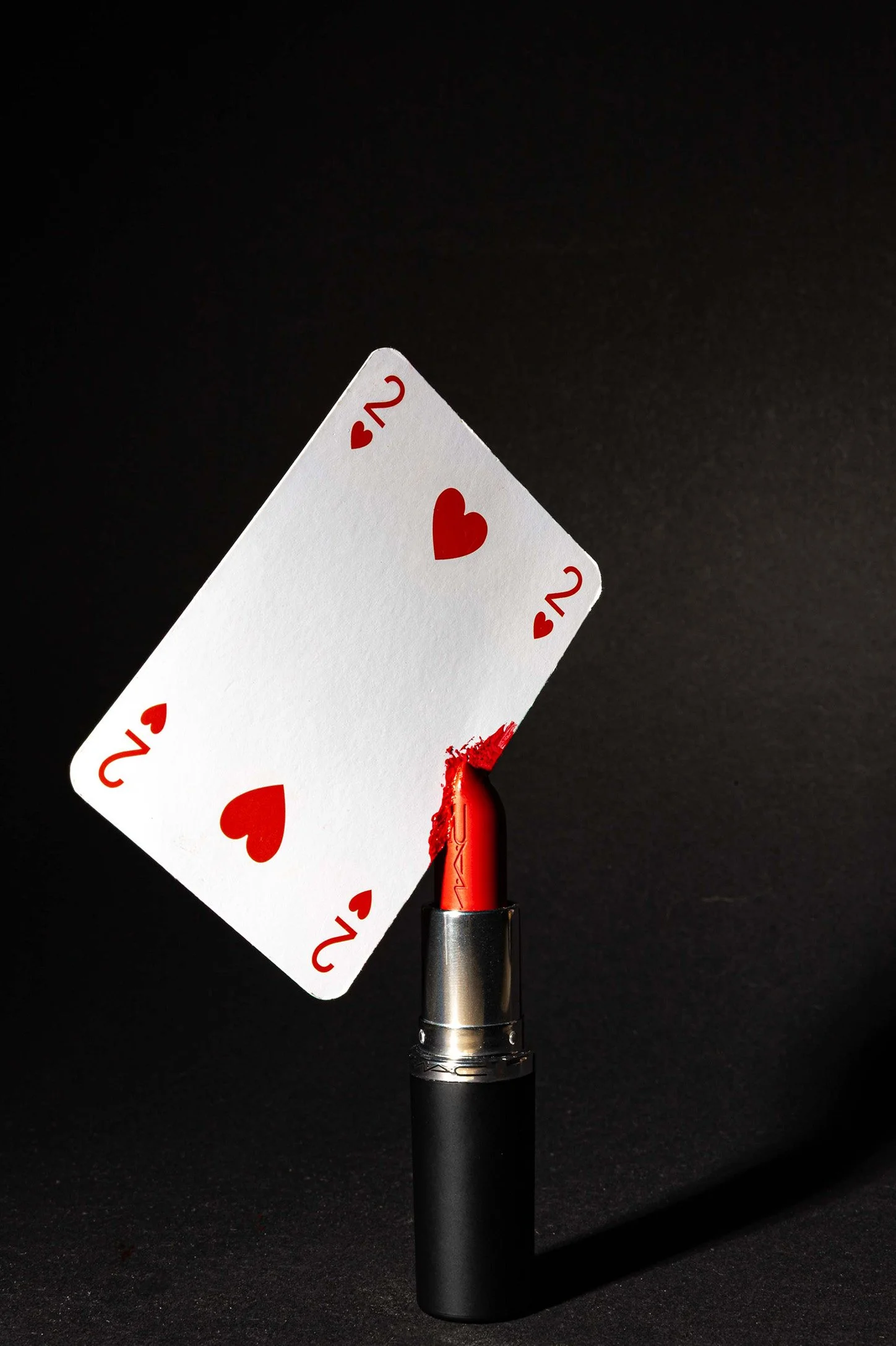 Harten twee speelkaart in een rode lippenstift gestoken tegen zwarte achtergrond – creatieve beauty productfotografie studio