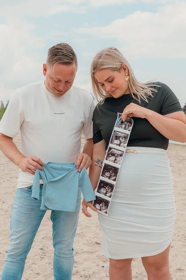 Koppel op het strand met echo foto’s en babykleertjes – zwangerschap aankondiging fotoshoot strand