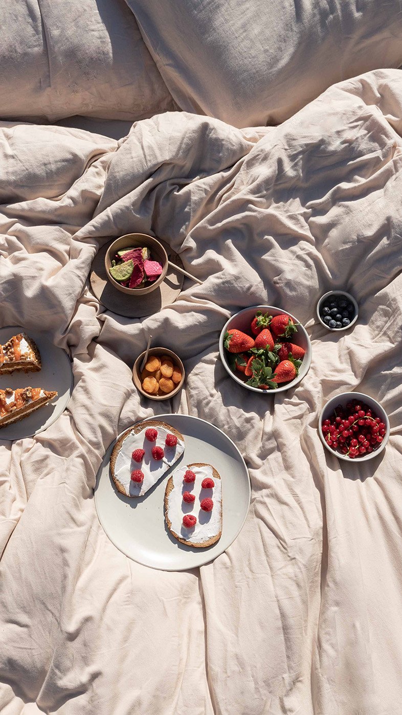 Picnic setting gestyled op beige bedsprei met brood, aardbeien, bosbessen en rode bessen – food styling en productfotografie