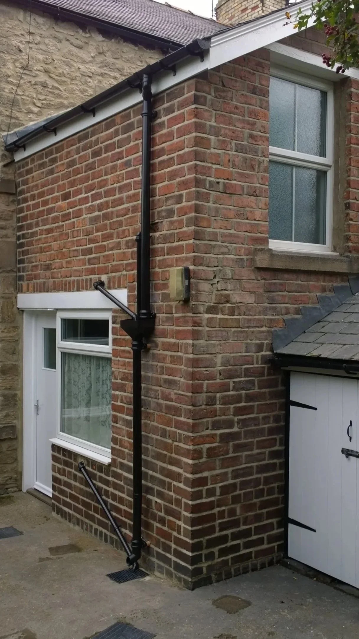 Close-up of an exterior brick house wall, newly repointed, with a black rain gutter system and downspout.