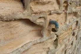 Close-up of a brick wall with a blue pipe protruding from it.