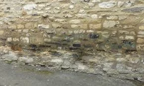 Close-up of a weathered stone brick wall with a rough-textured surface and some mortar between the bricks.
