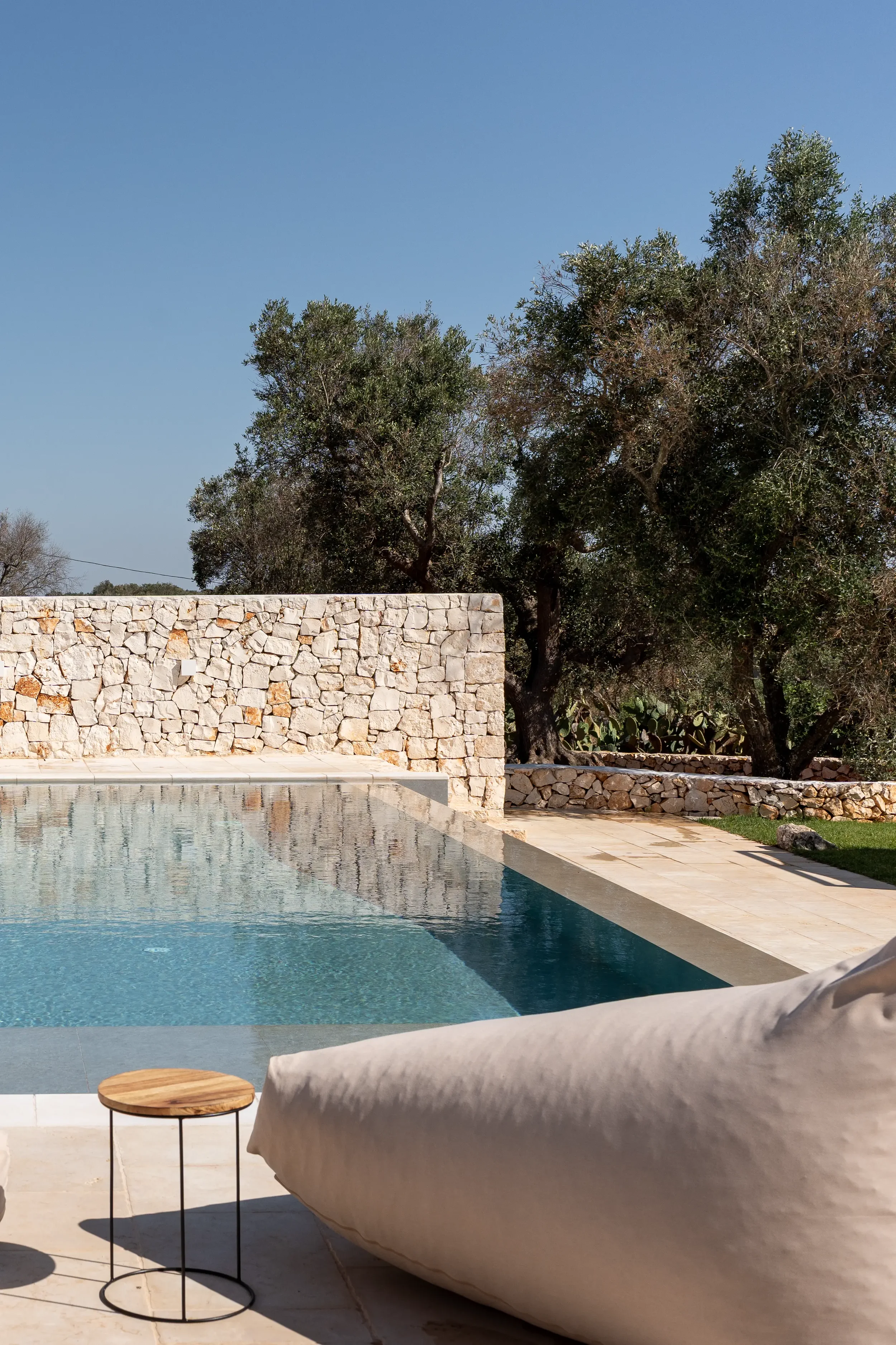 Ein Swimmingpool mit Steinen umgeben, im Hintergrund Bäume und ein blauer Himmel.