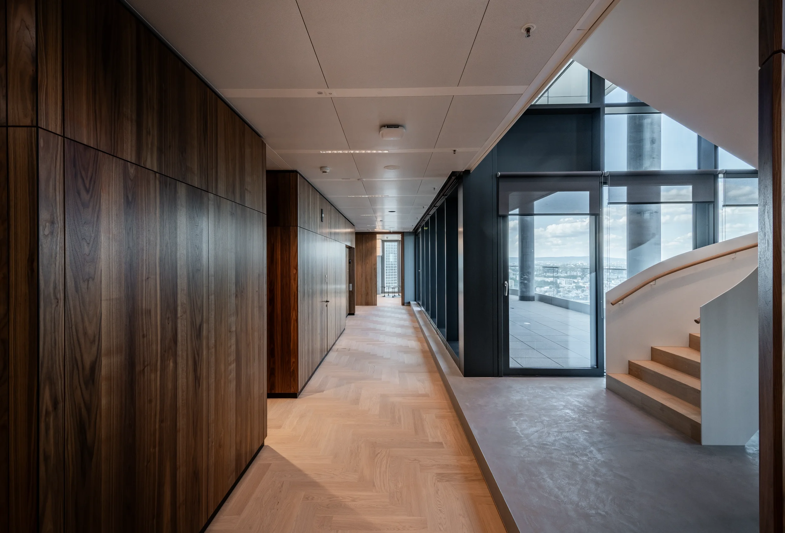 Innenansicht eines modernen Gebäudes mit Holzwänden, großen Fenstern und steilem Treppenaufgang