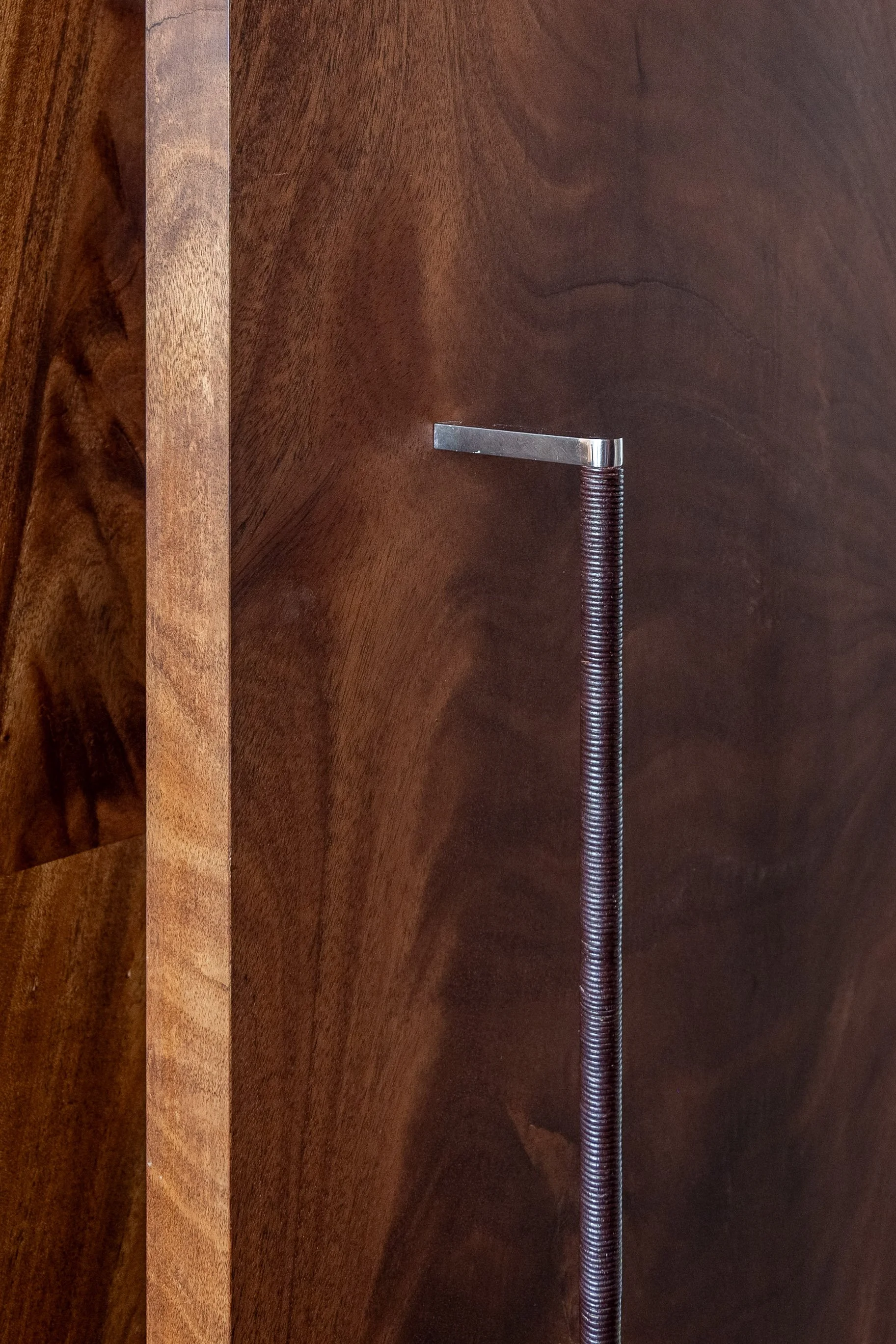 Ein Möbelstück aus dunklem Holz mit einer Spindel oder Zylinder aus Metall, das an der Seite befestigt ist.