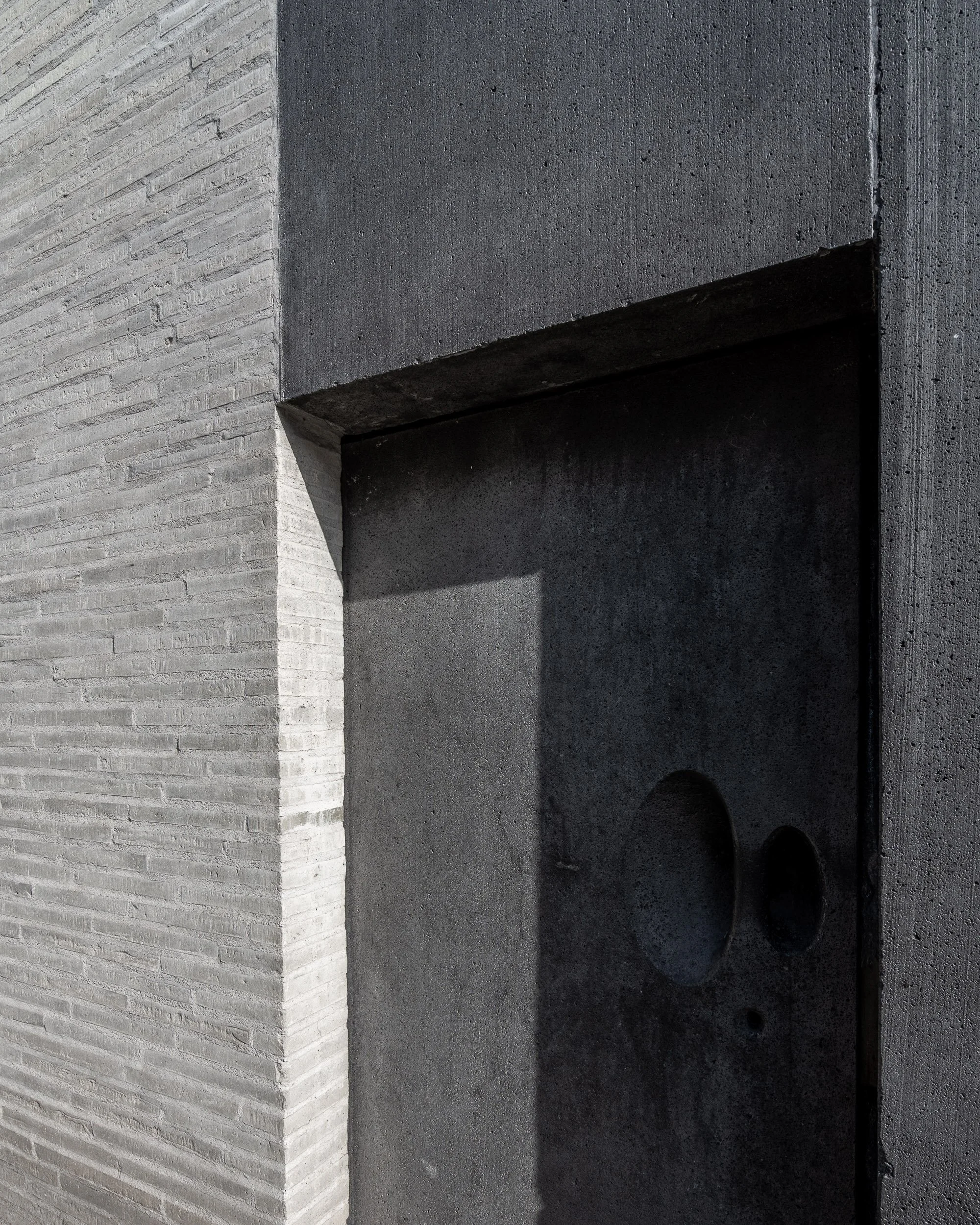 Nahaufnahme einer Wand mit unterschiedlichen Oberflächen, bestehend aus hellen, gerippten und dunklen, glatten Steinen, mit hellen und dunklen Schatten.