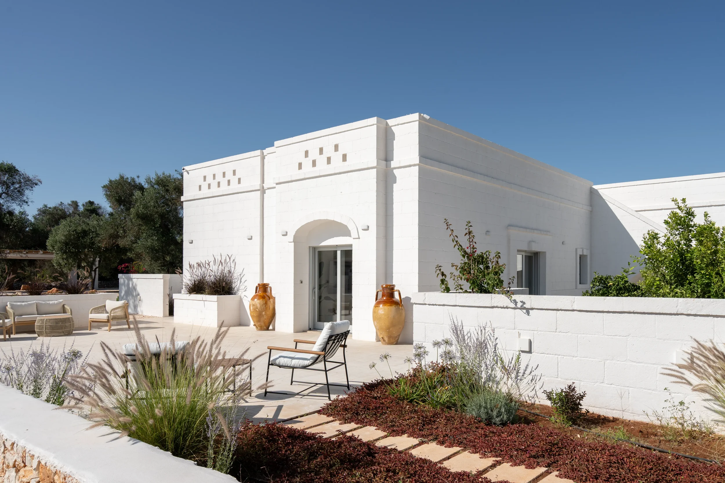 Weißes Haus mit Terrassenmöbeln und großen Töpfen vor einer blauen Himmel