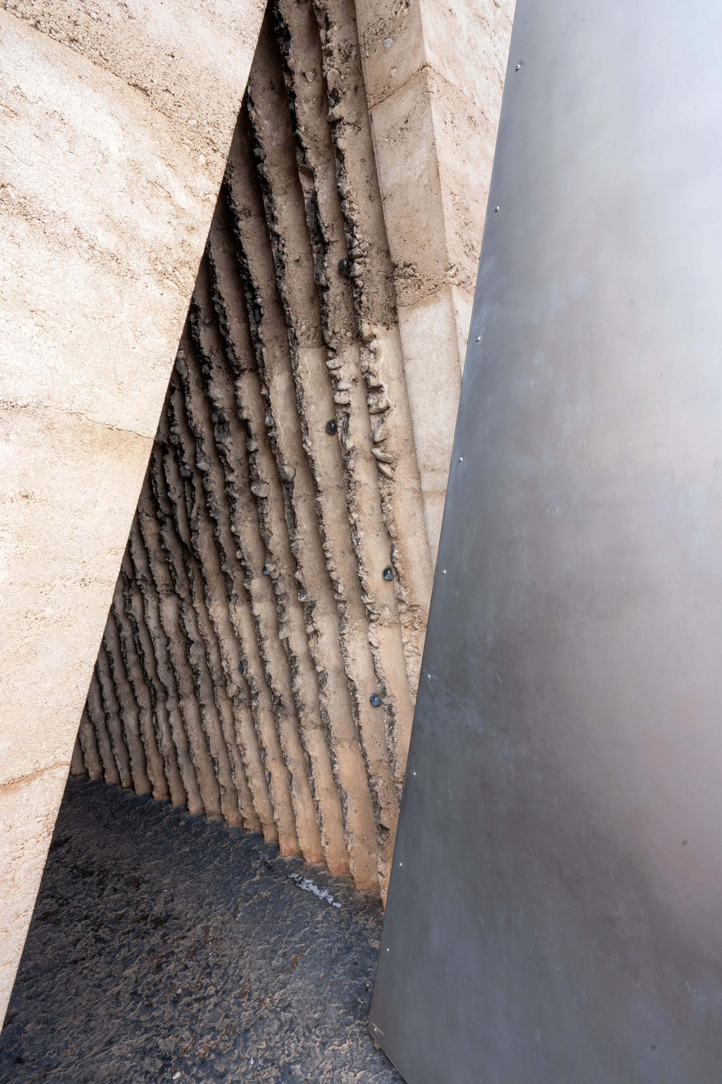 Bruder Klaus Feldkapelle von Peter Zumthor, Schalwand mit isolierendem Material in vertikalen Nuten, teilweise verdeckt durch eine metallene Verkleidung.