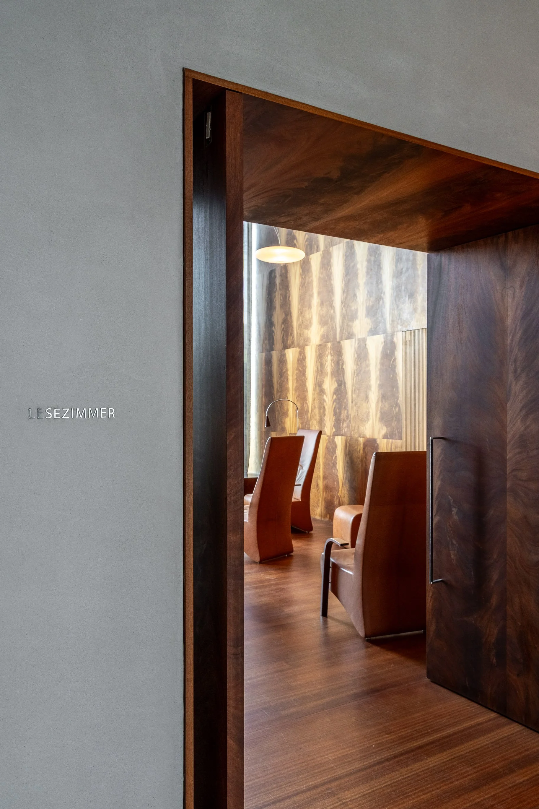 Blick in einen Leseraum mit Holzmöbeln und einer goldfarbenen Wand, durch eine Türöffnung sichtbar, mit dem Schriftzug 'LESERZIMMER' an der Wand neben der Tür.