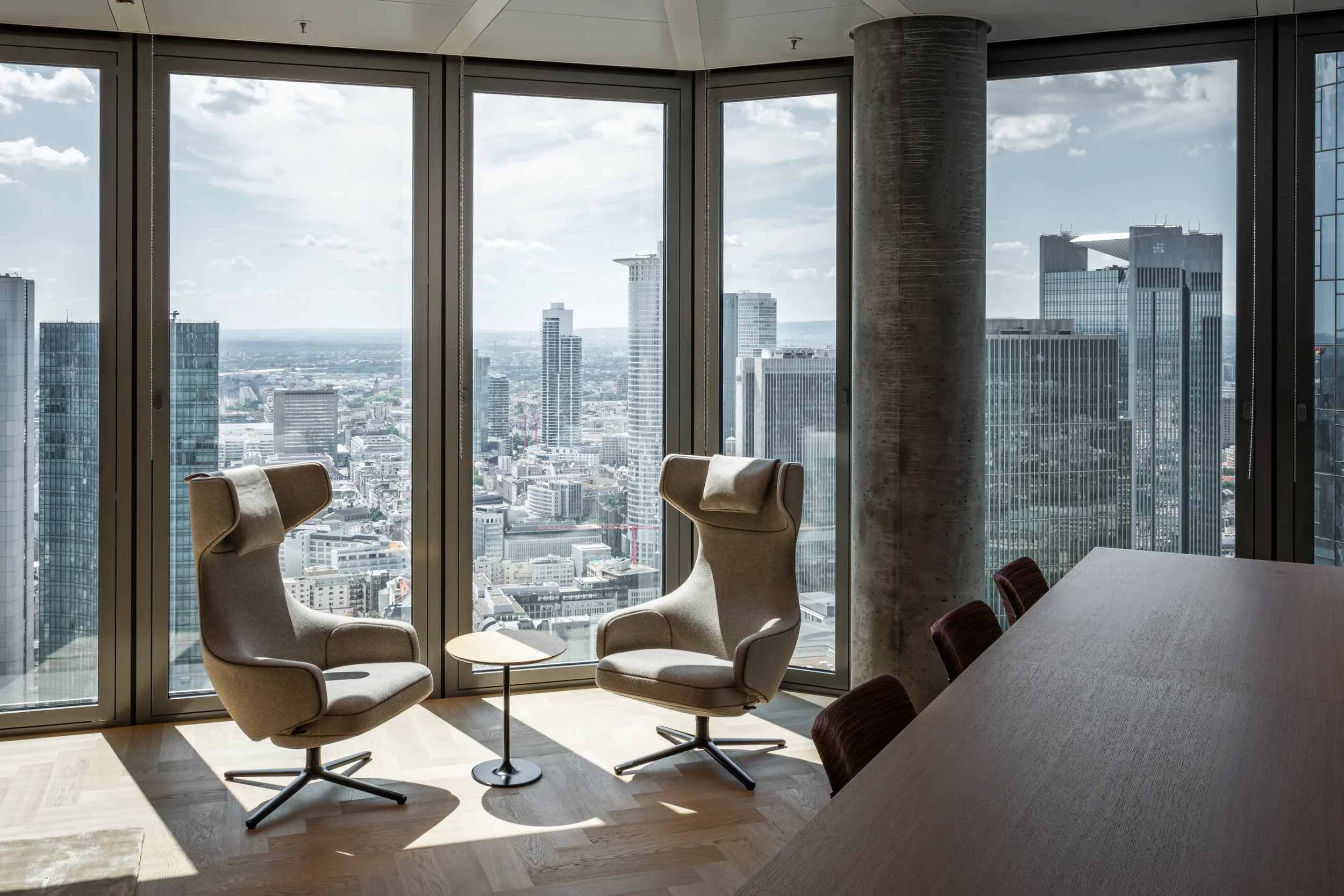 FOUR Frankfurt T4, Zwei bequeme Sessel vor großen Fenster mit Blick auf eine städtische Skyline bei Tag.