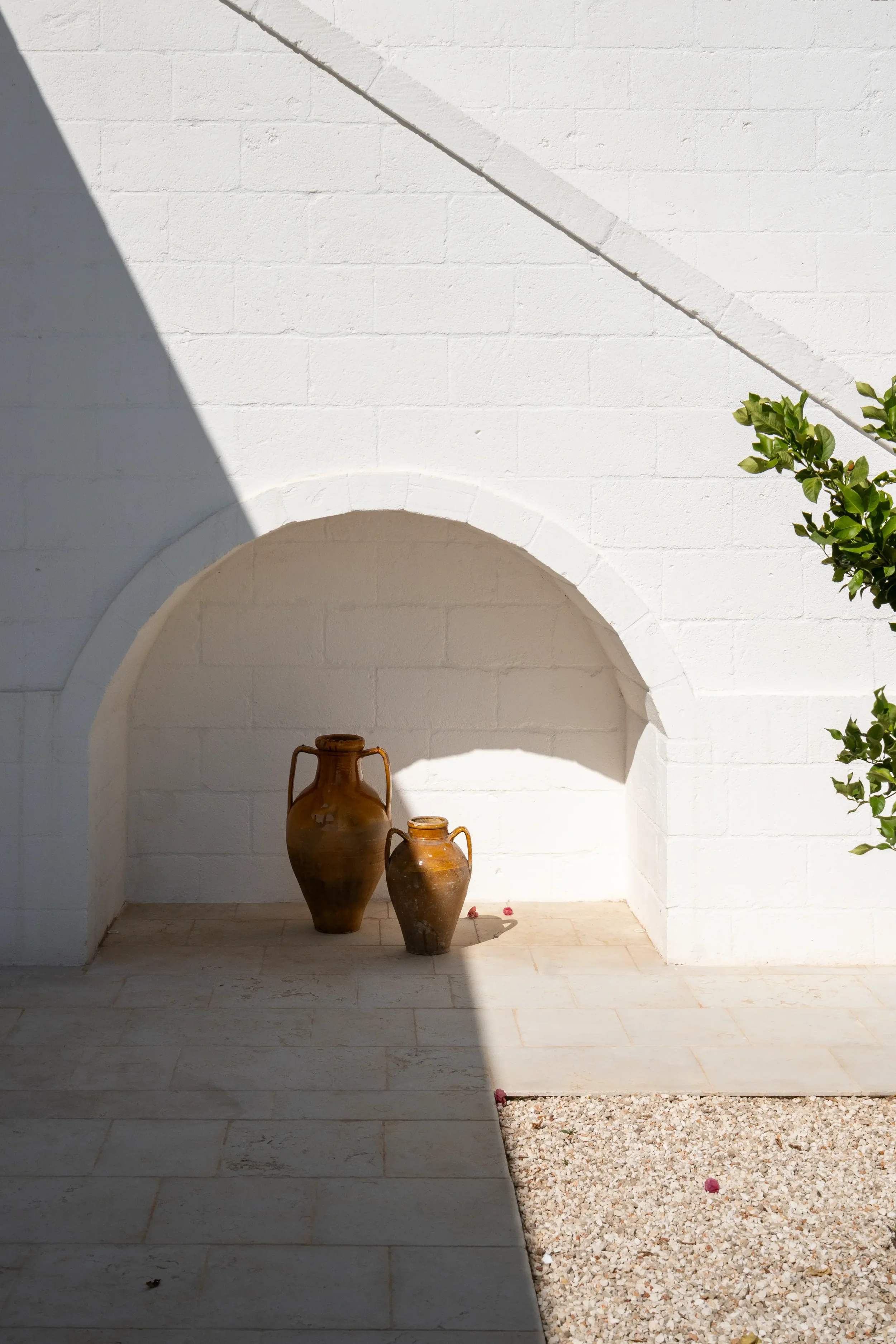 Zwei braune Tongefäße stehen in einem weißen, größtenteils im Schatten liegenden Nische vor einer weißen Ziegelmauer.