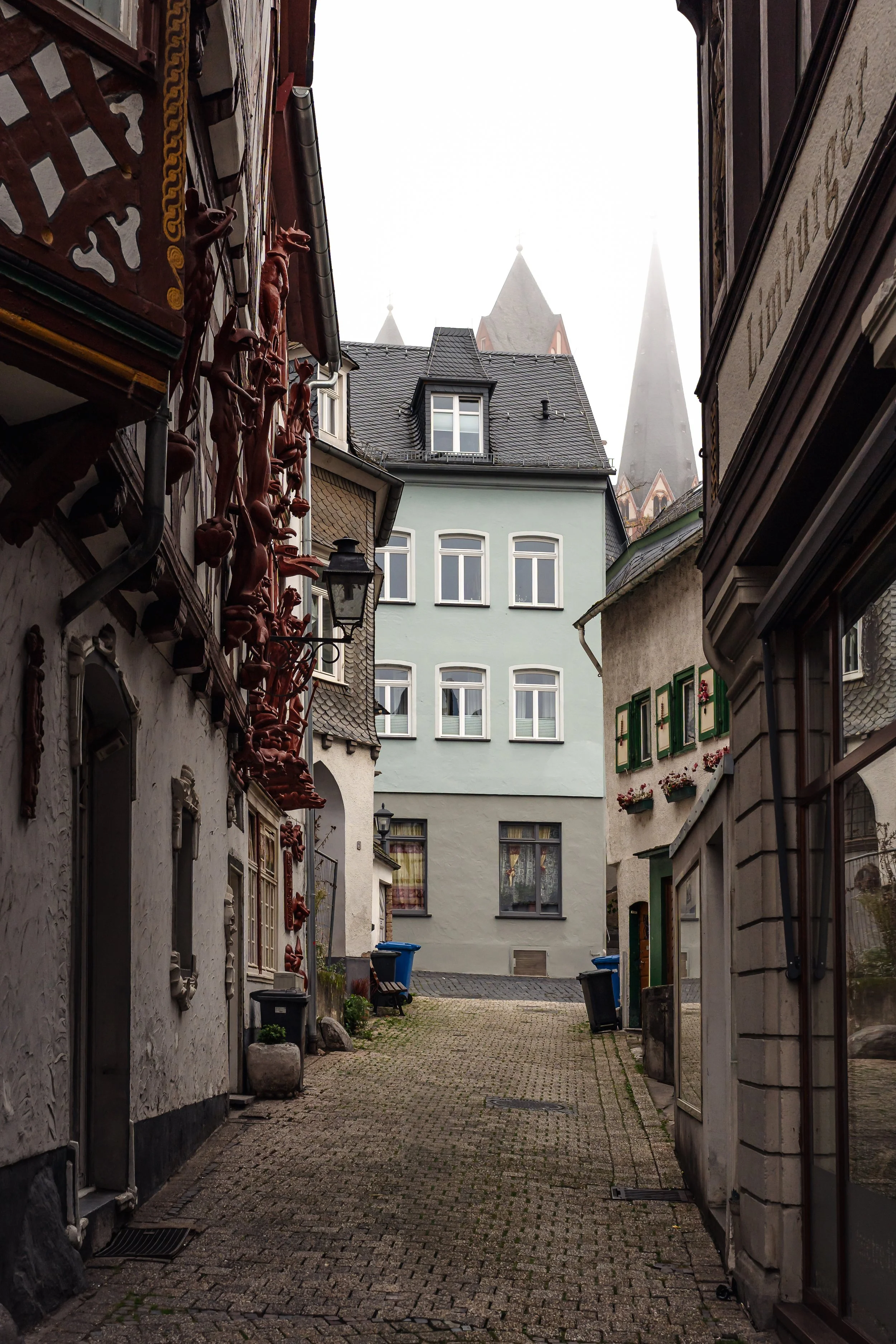 Ältere Gebäude und enge Gasse in einer europäischen Stadt, nebliger Himmel, freundliche Atmosphäre.