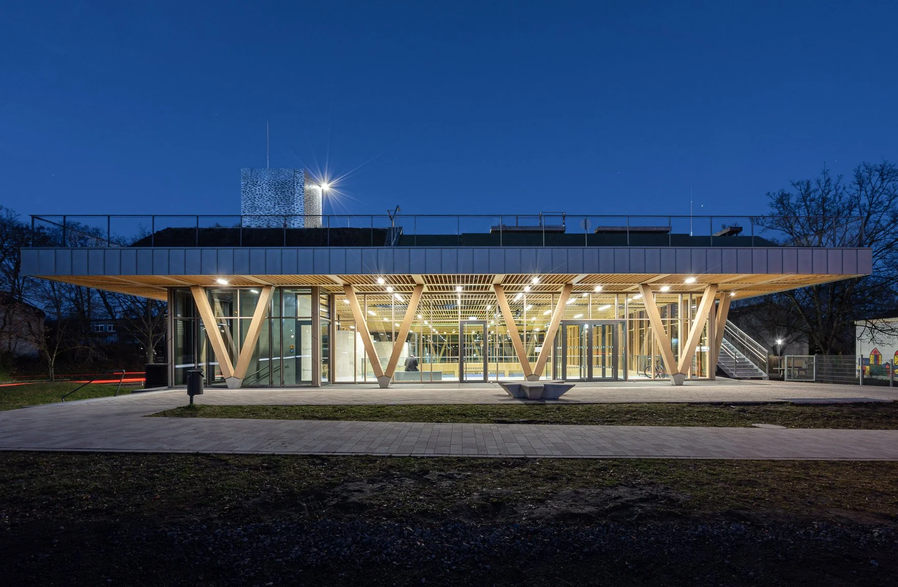 Modernes zweistöckiges Gebäude mit großen Glasfenstern und Holzstützen, frontal ansicht während der Abenddämmerung