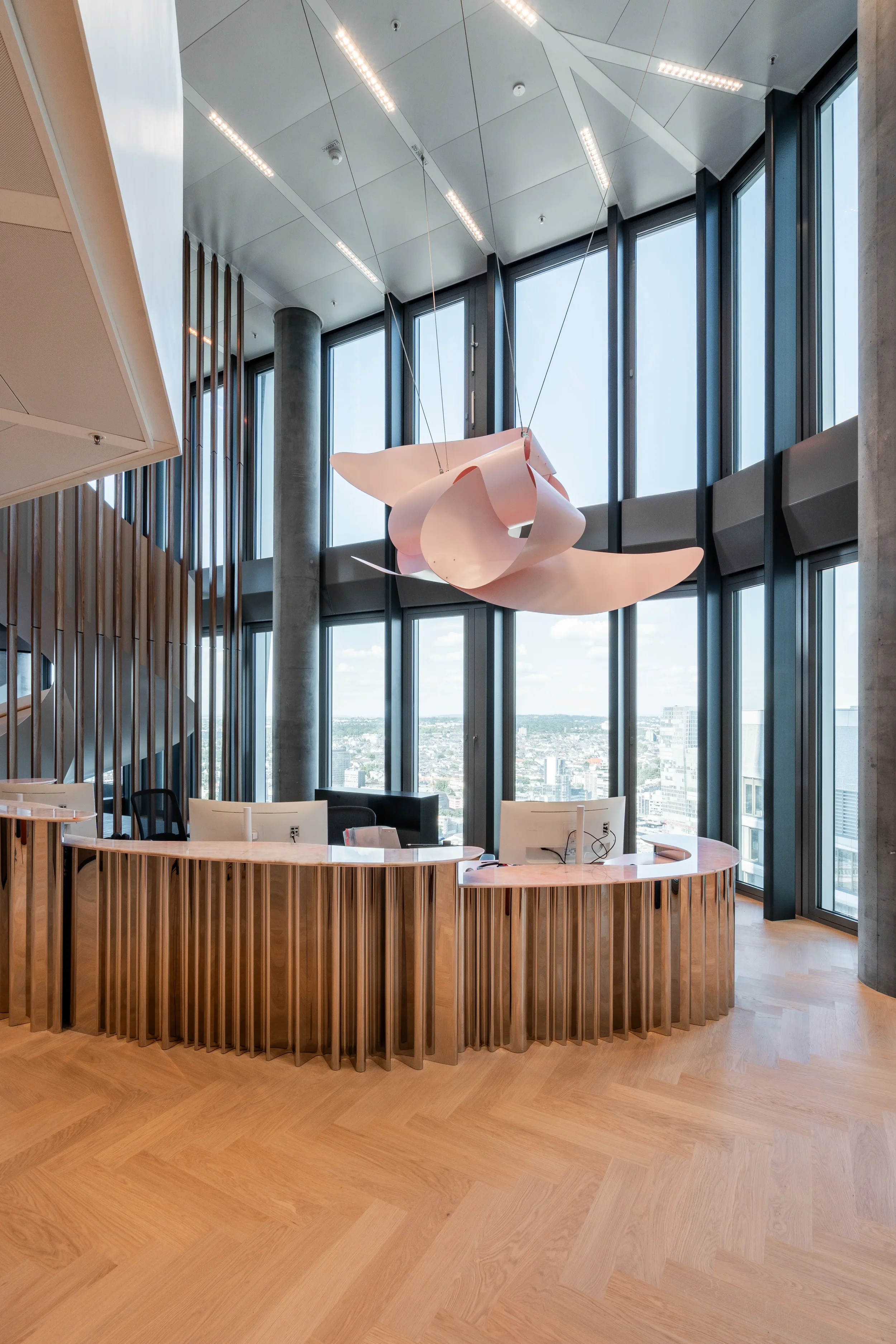 Modernes Empfangs- oder Rezeptionstresen in einem hohen, lichtdurchfluteten Raum mit hohen Fenstern und einer abstrakten Deckenleuchte.