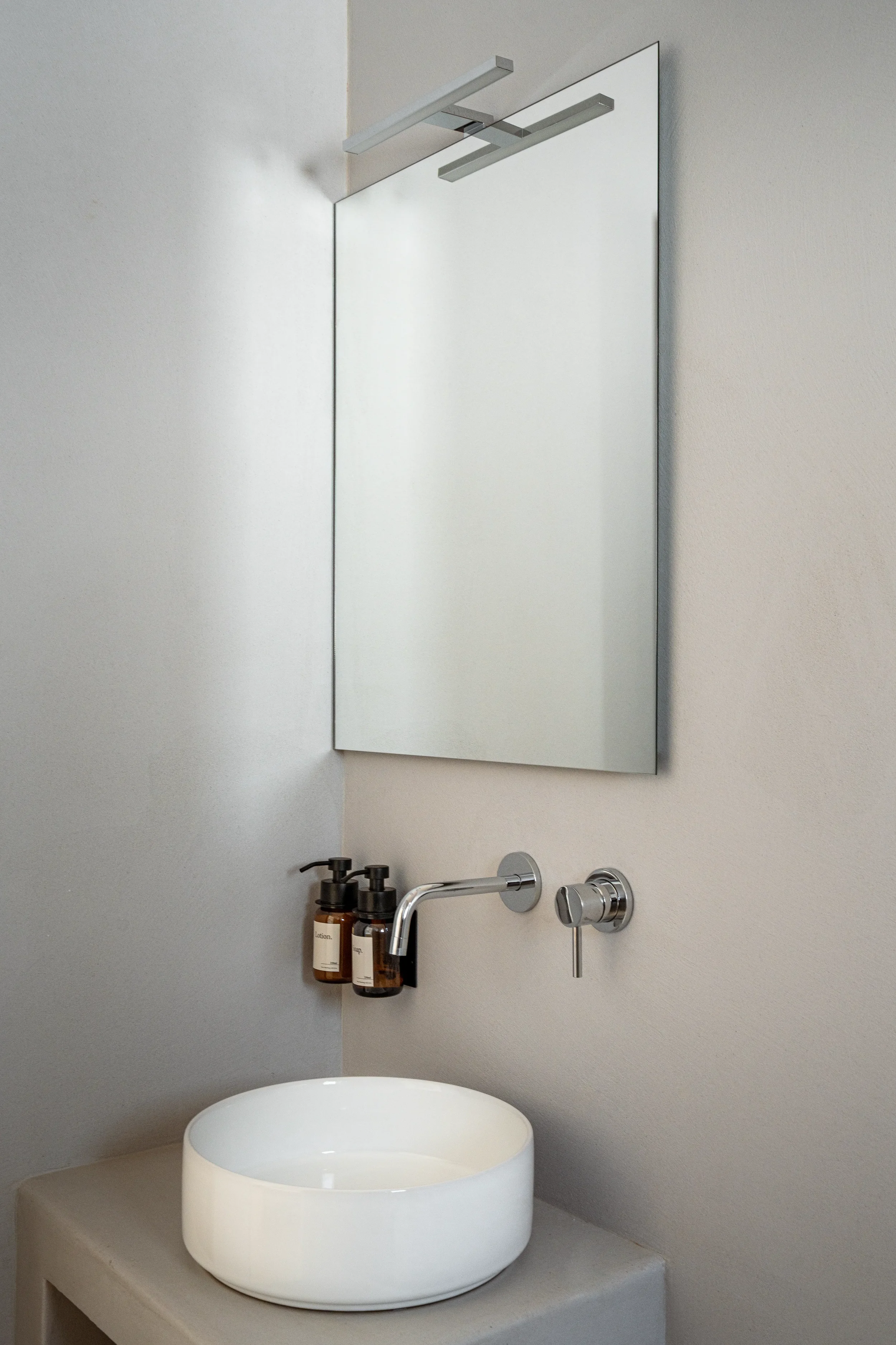 Moderner Waschraum mit weißem, runden Waschbecken, Spiegel, Seifenspendern an der Wand, Wasserhahn und Badelement