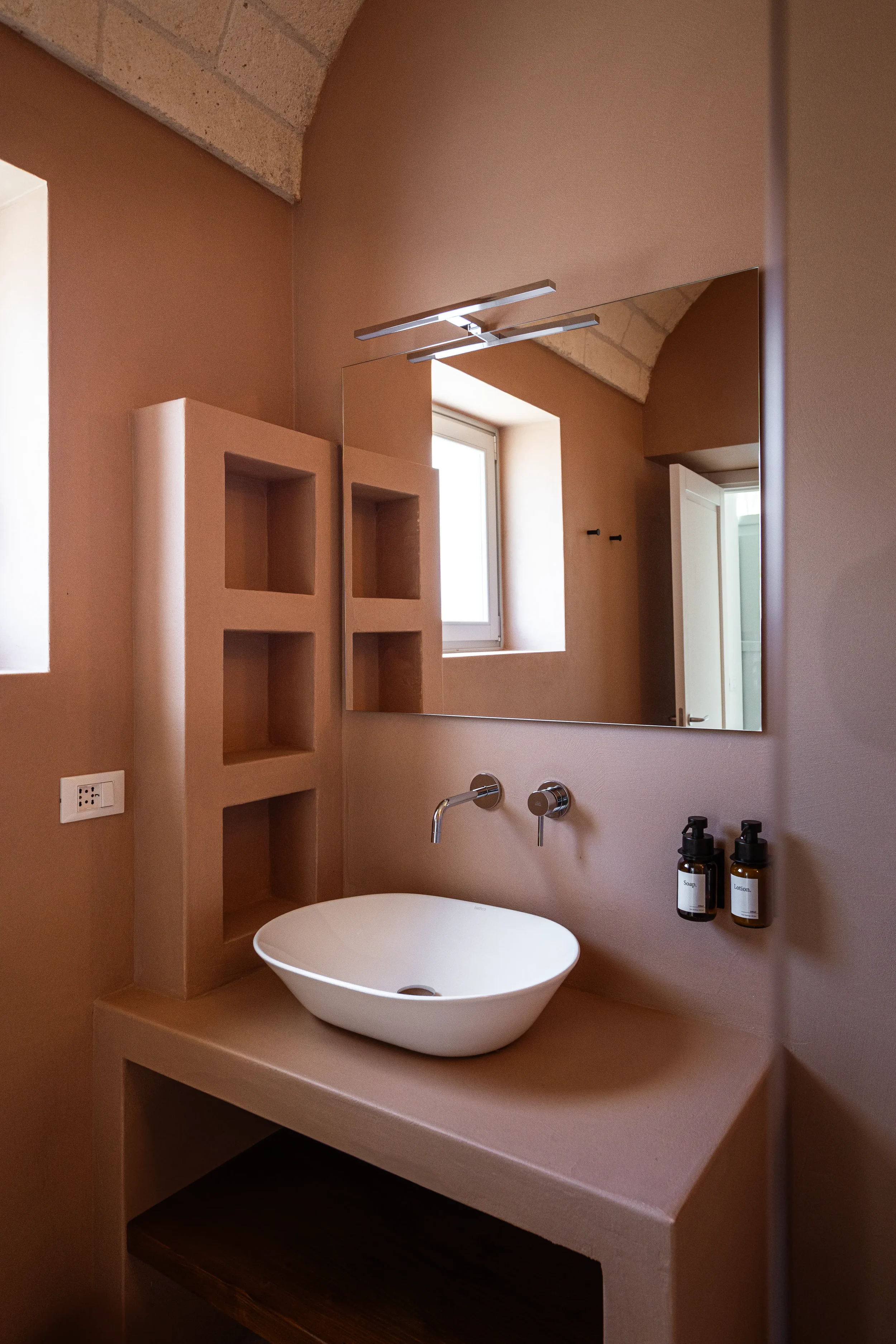 Ein modernes Badezimmer mit einem großen rechteckigen Spiegel, einem weißen ovalen Waschbecken, beige Wänden und kleinen Fenstern.