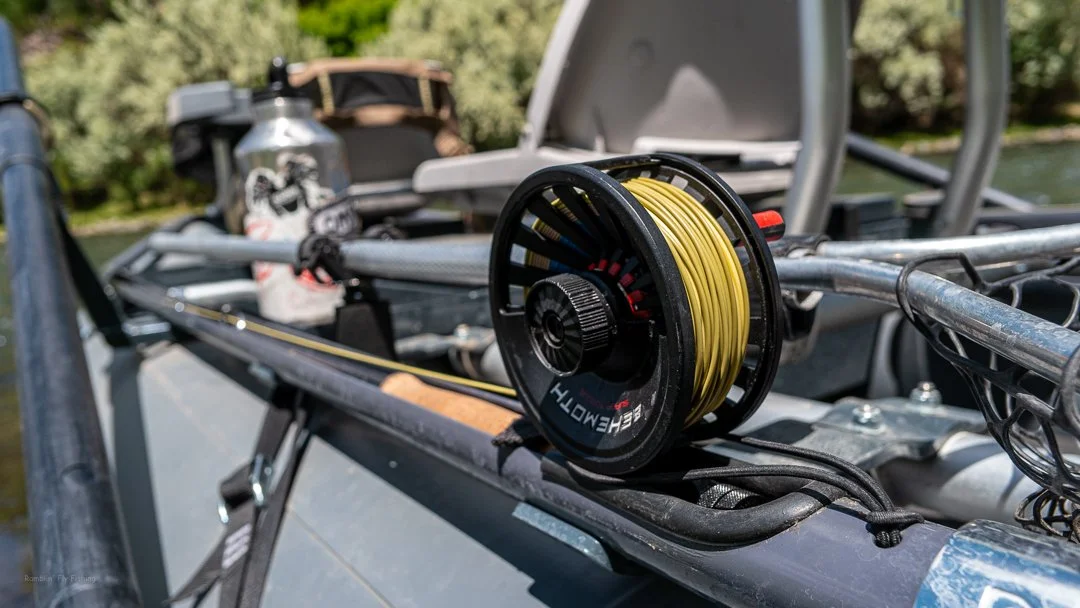 A fishing reel spool with yellow fishing line on a boat, with fishing gear and a water bottle in the background.