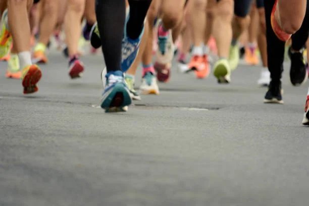 A group of runners participating in a race, viewed from the ground level showing their colorful running shoes and legs.