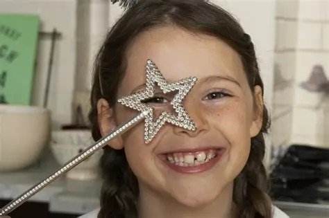 A girl holding a star-shaped magic wand over her eye, smiling.