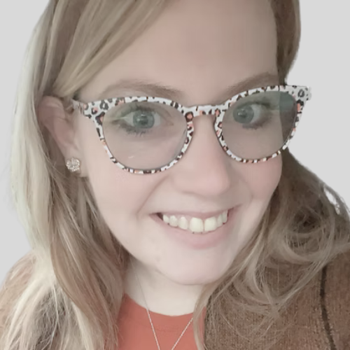 A woman smiling with blonde hair, wearing leopard print glasses, earrings, and a necklace.