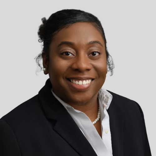 Professional portrait of a smiling African American woman wearing a black blazer and white shirt against a gray background.