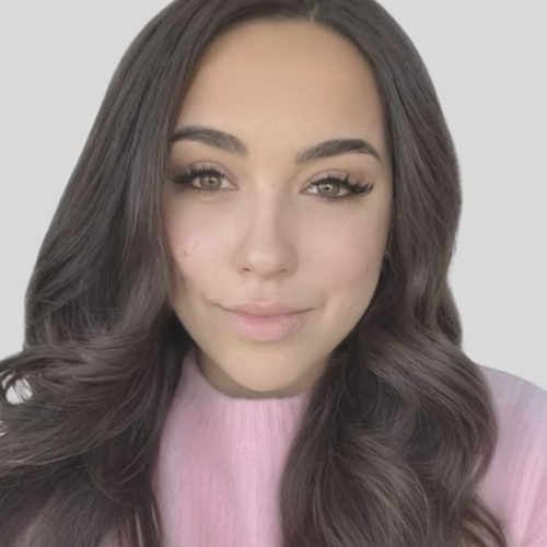 A woman with long, wavy brown hair and makeup, wearing a pink top, winking at the camera.