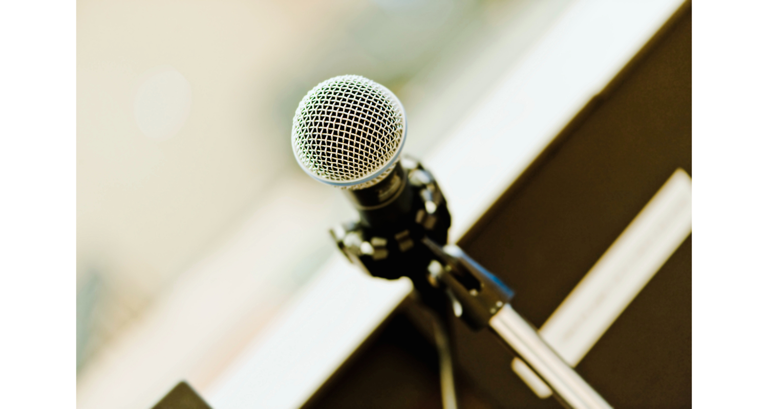 Close-up of a microphone mounted on a stand, positioned near a window with blurred background.