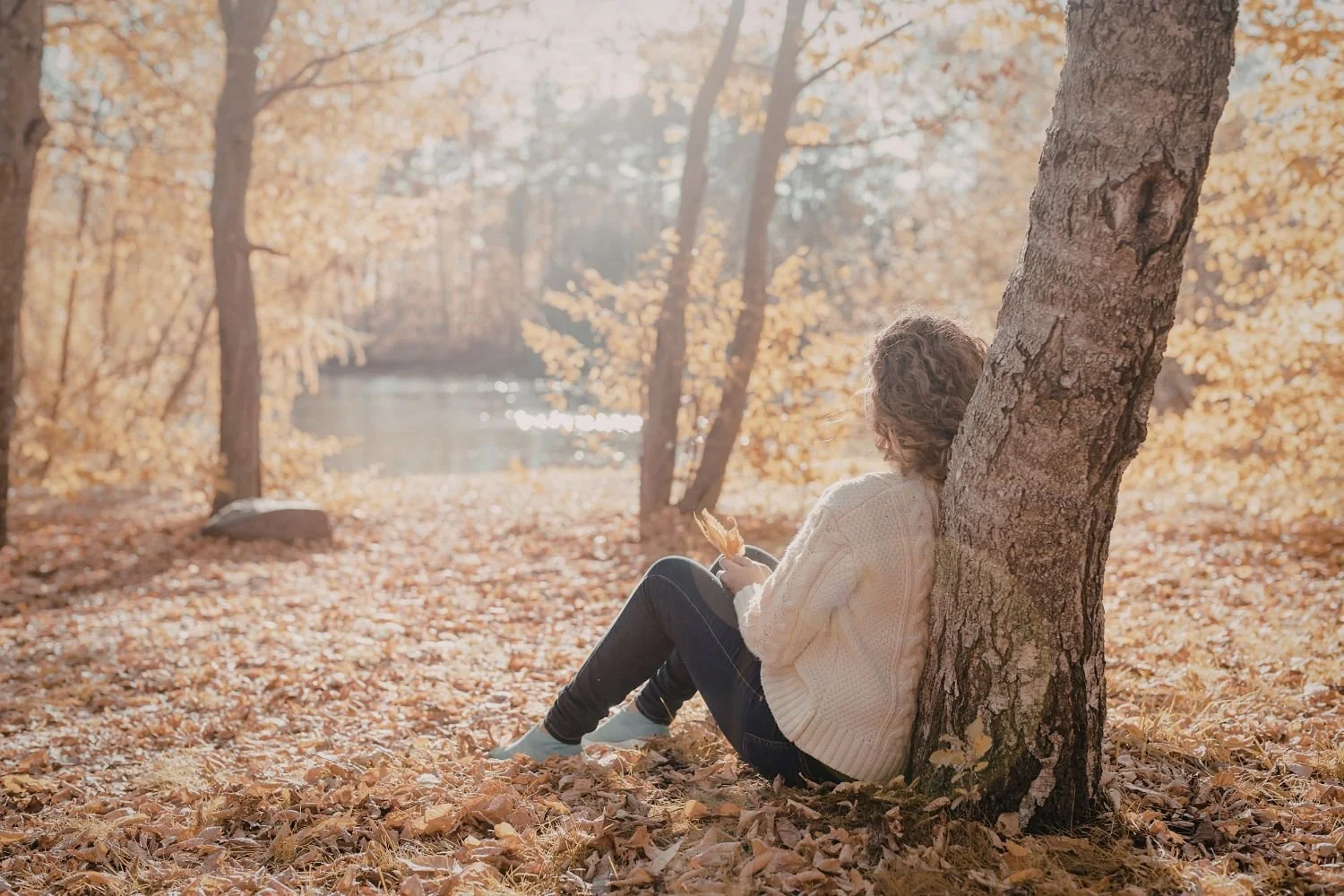 Woman sitting on the forest floor leaning against a tree