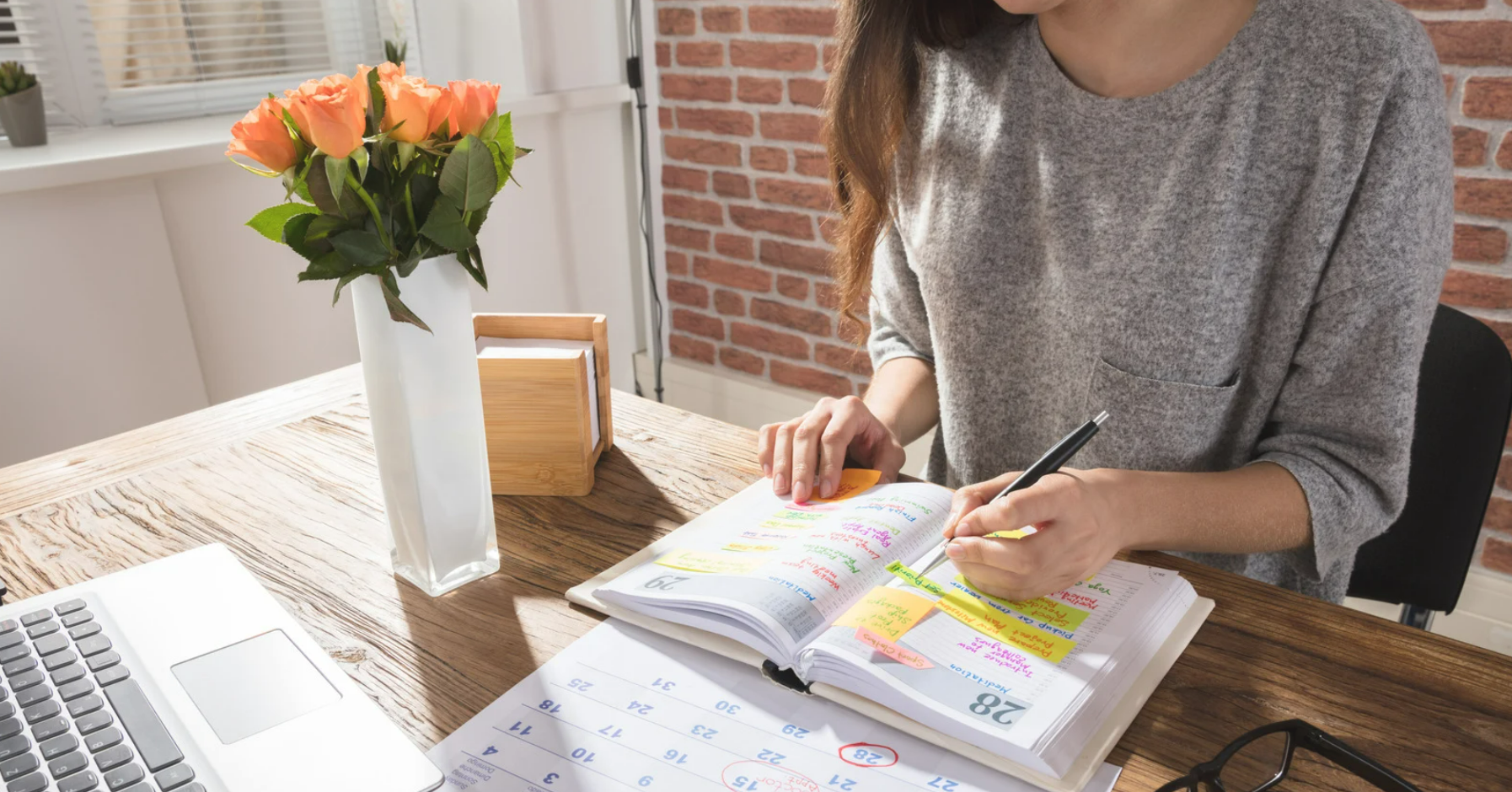 Woman sitting at a desk with roses on the table. She is at home with a planner and a pen in her hand.