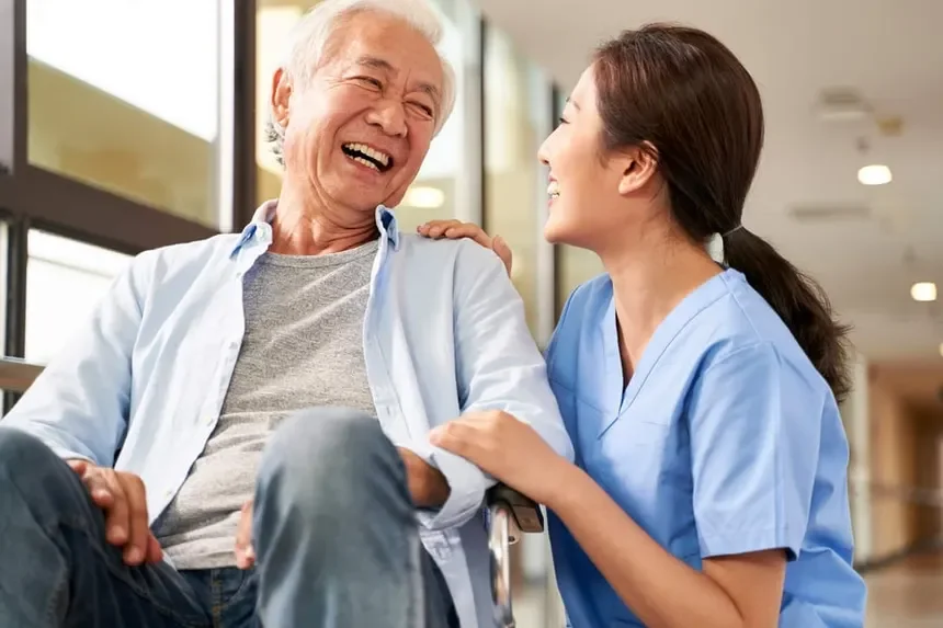 A caregiver and an elderly man are laughing and smiling at each other