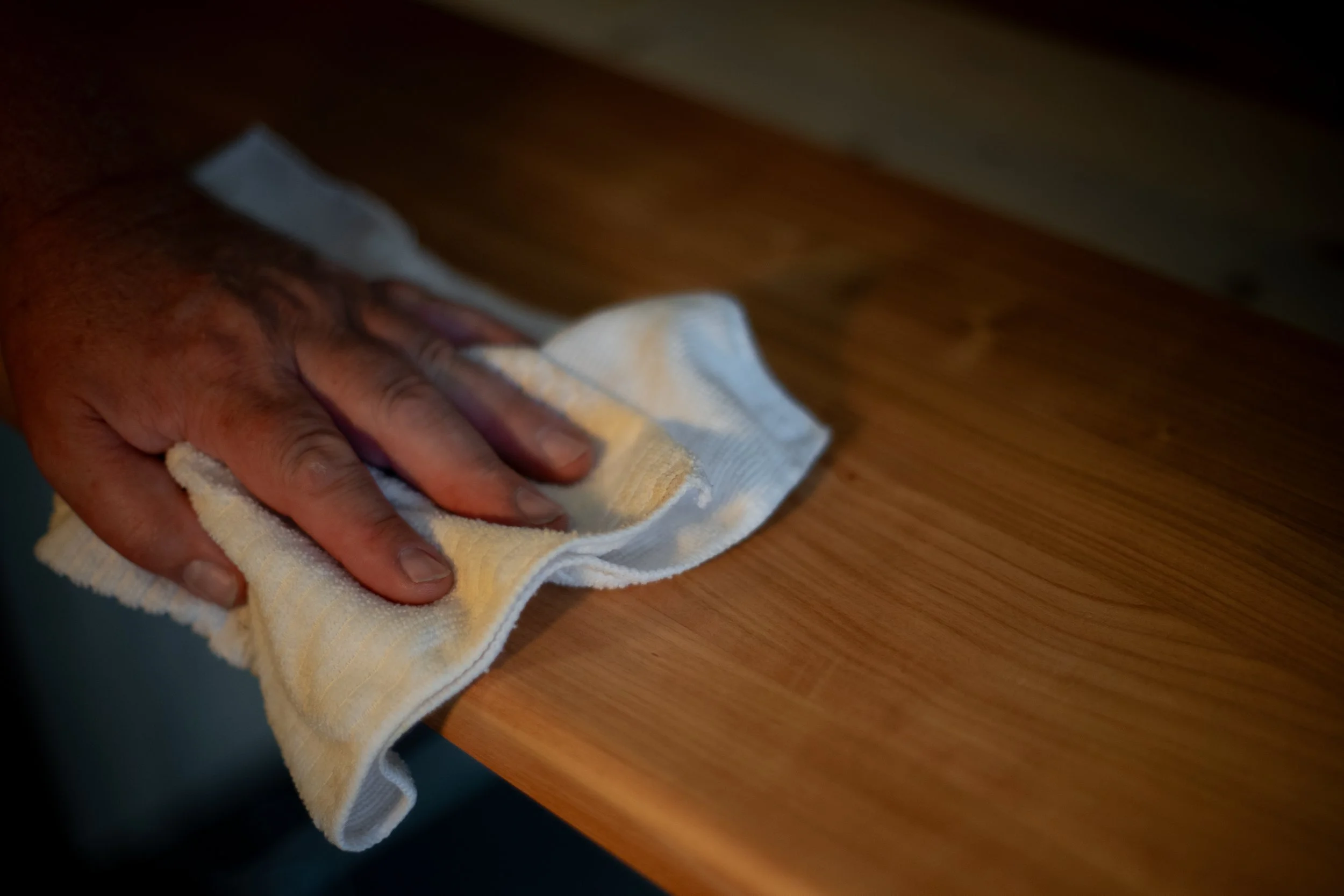 A person's hand wiping a wooden surface with a yellow and white cloth.