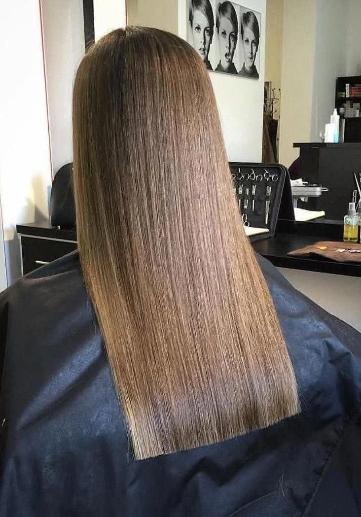 Back of a woman with long, straight, shiny brown hair in a hair salon.