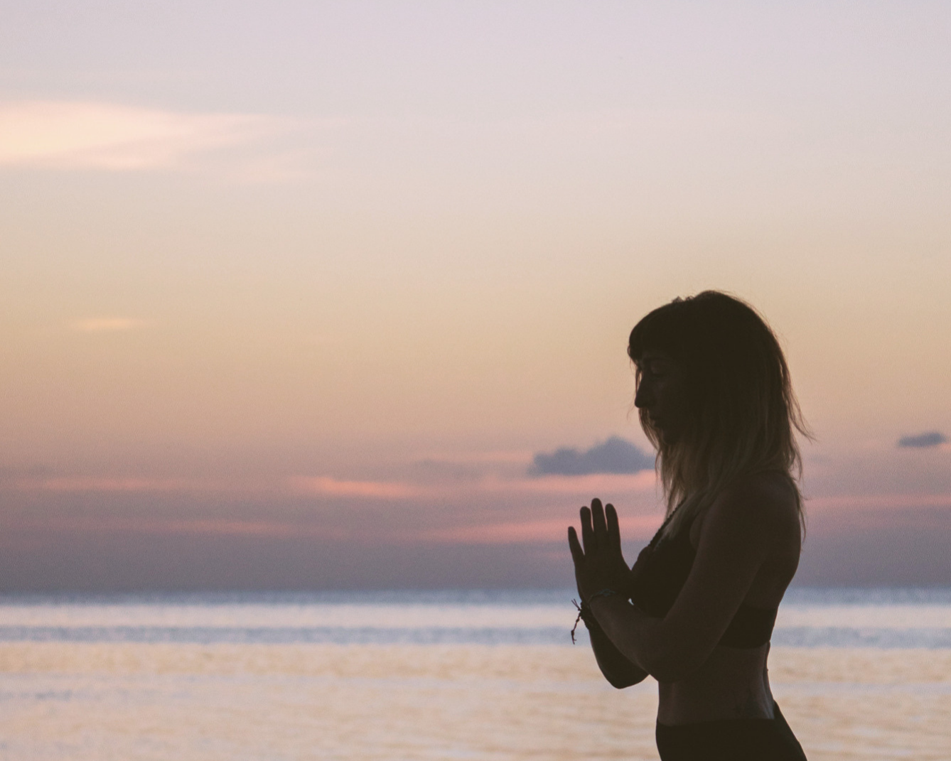 A silhouette of a woman practicing yoga or meditation on the beach at sunset.