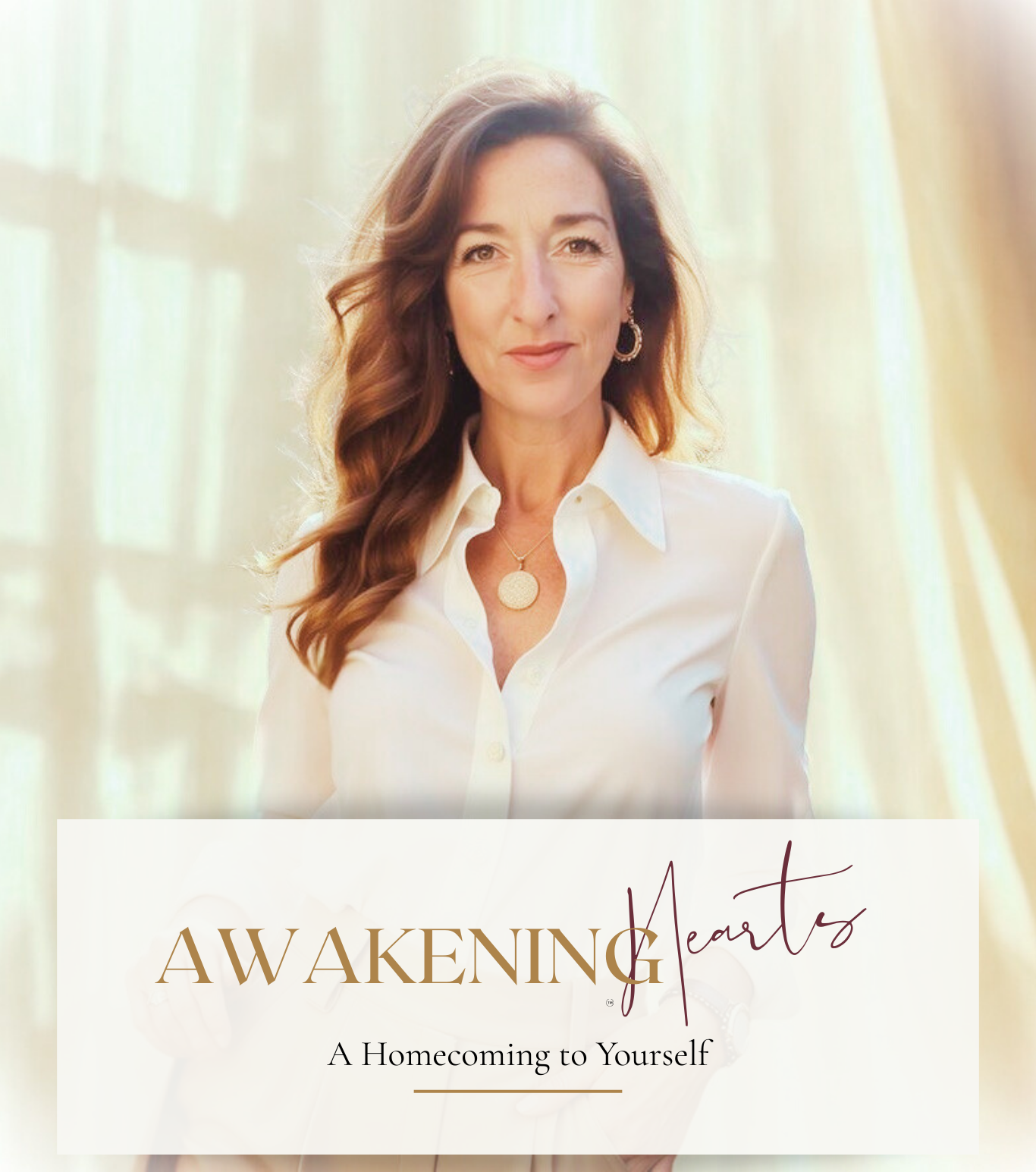 A woman with long red hair, wearing a white shirt, gold jewelry, and a necklace, stands in front of a light, airy background with soft sunlight.