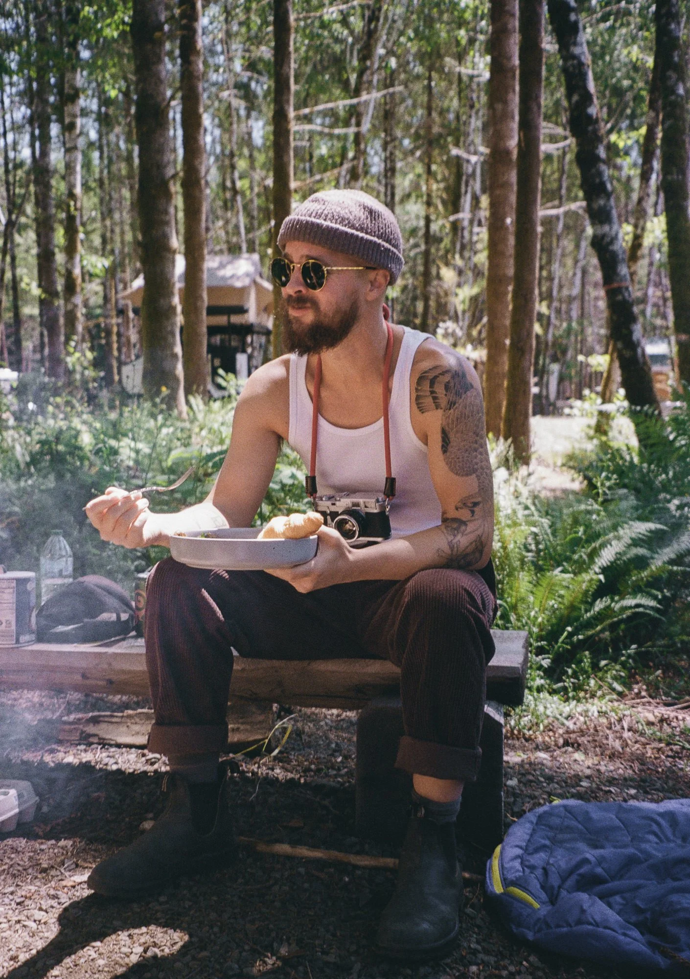 photographer eating around campfire with leica camera dangling from neck