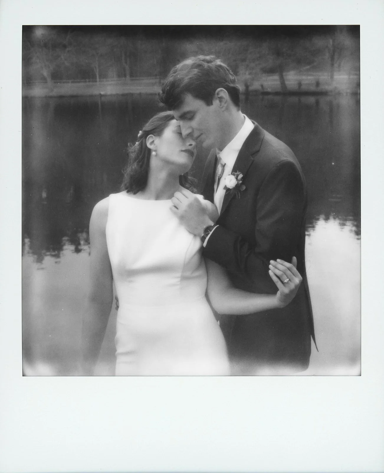 polaroid wedding photo of couple embracing in front of lake