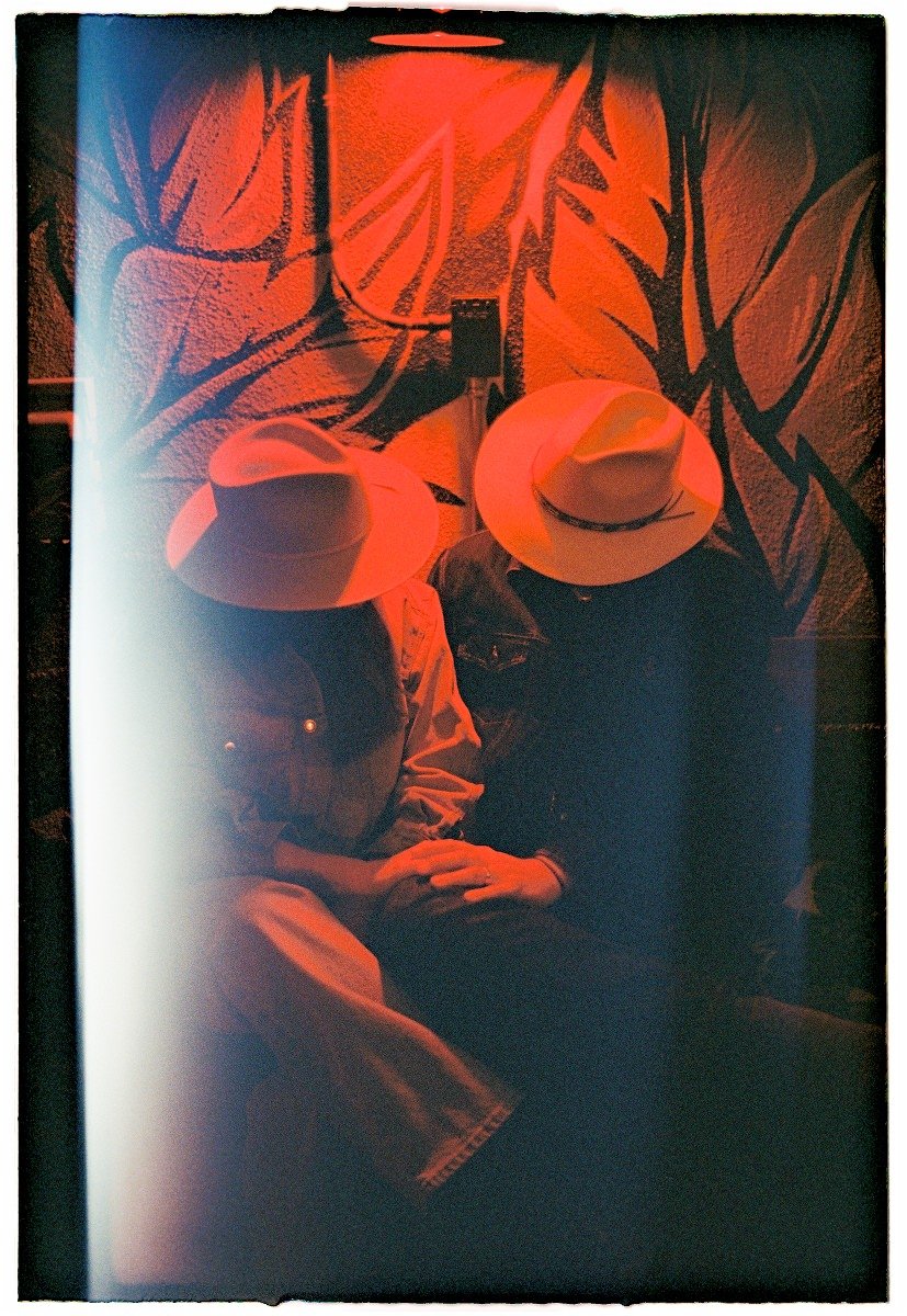 a couple sitting under red light with cowboy hats and holding hands