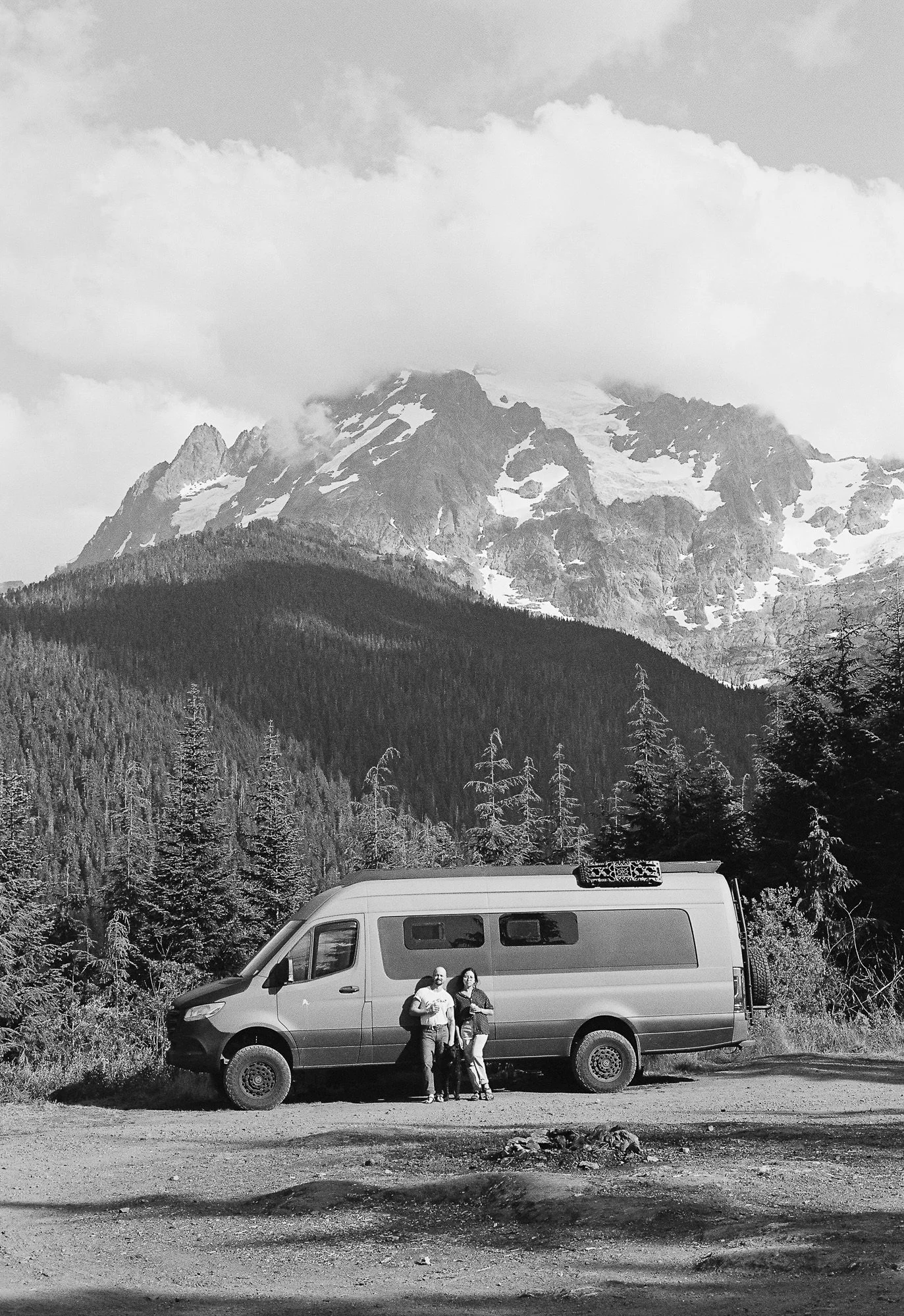 self portrait of couple standing in front of sprinter van with mount baker in the background