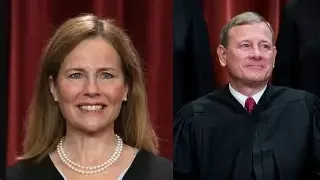 A woman with long brown hair wearing a pearl necklace and a black top, standing next to a man in a judge's robe with a red tie, both smiling.
