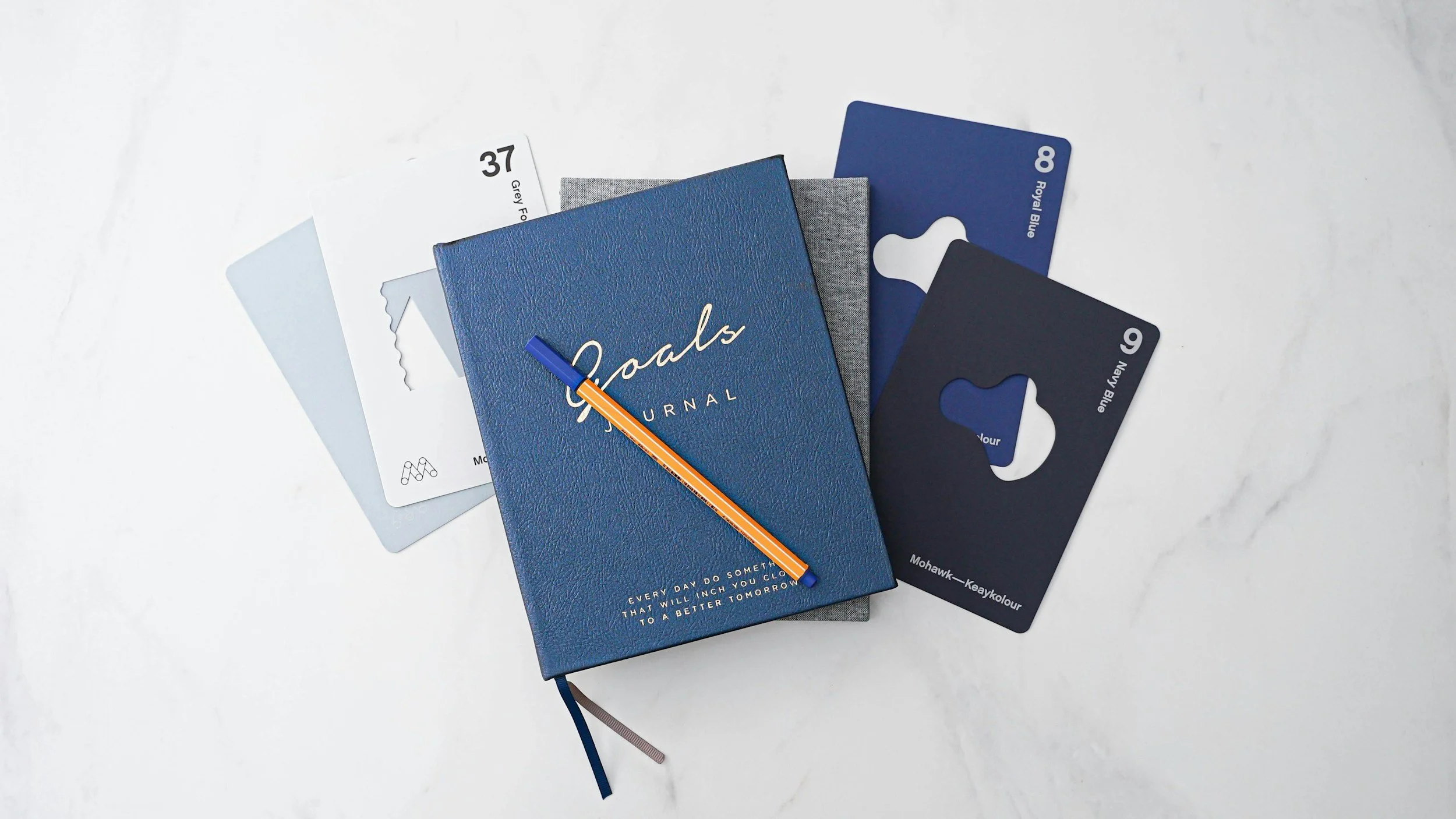 Blue journal, sticky notes with color labels, and an orange pen on a white surface.