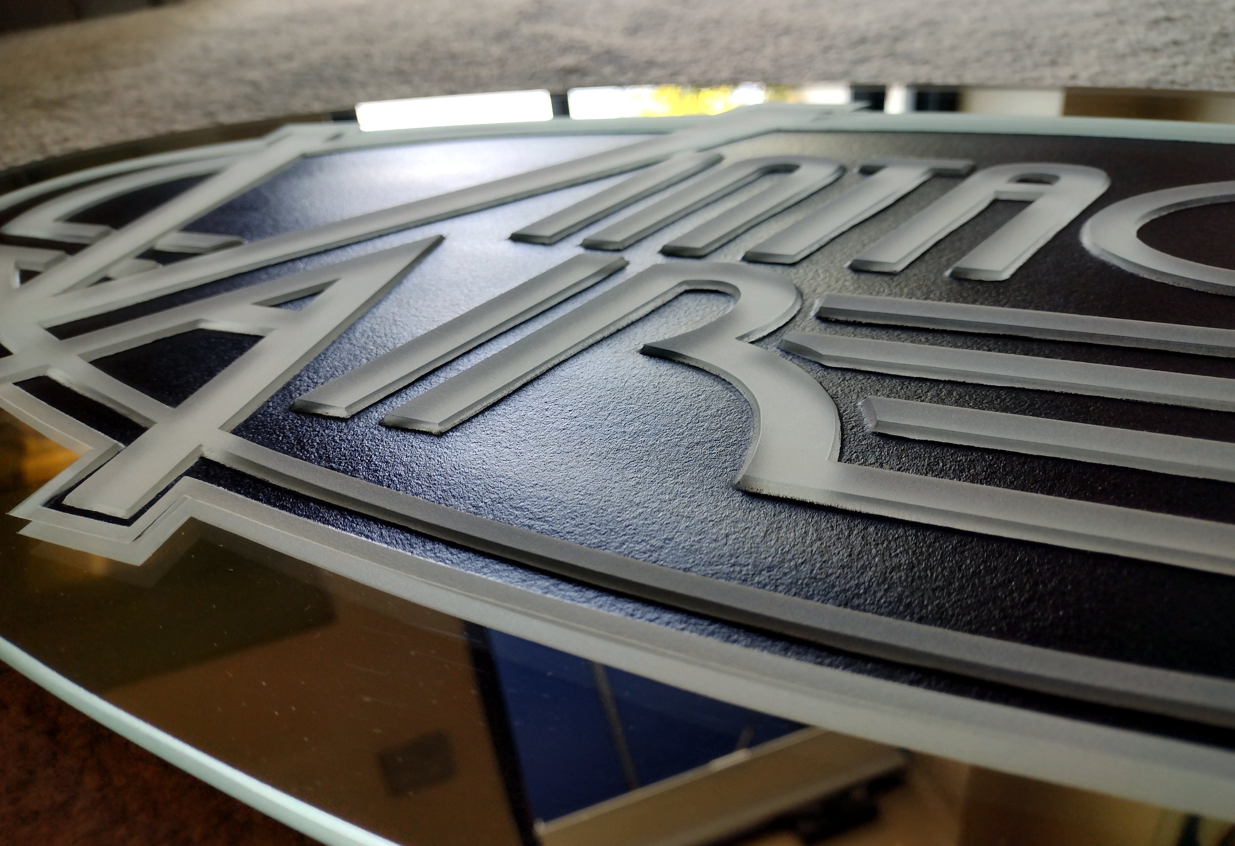Close-up of a metallic 3D badge with the word 'Harley Davidson' embossed on a black textured background.