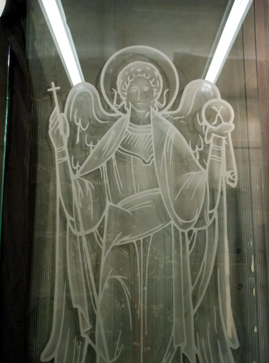 Decorative glass panel with a religious illustration of an angel holding a cross and a globe, rendered in white outline.