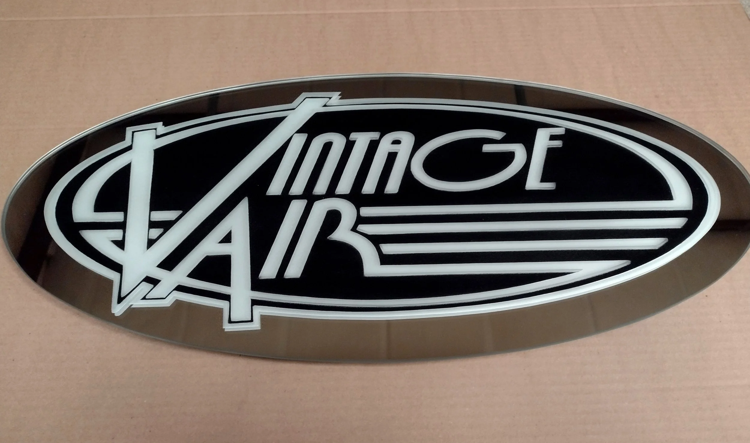 A sign resembling the Chevrolet Corvette logo with a black background, white outline, and the words 'Corvette' in stylized white lettering.