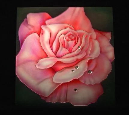 A realistic painting on dimensional carved glass of a pink and red rose with water droplets on its petals, set against a dark background.