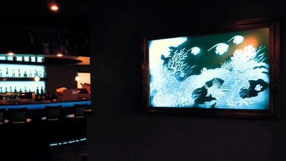 Brightly lit aquarium display with coral and fish images on a screen in a dimly lit bar or lounge area.