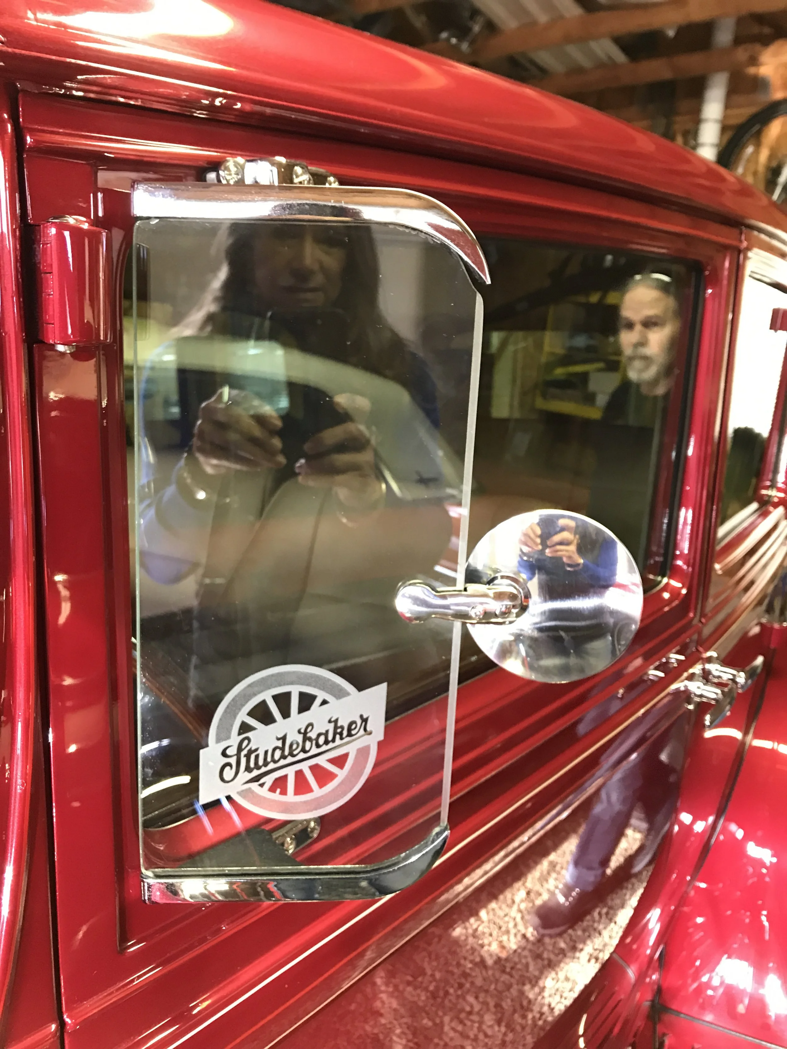 Close-up of etched glass on a vintage red Studebaker vehicle's window, inside a garage.
