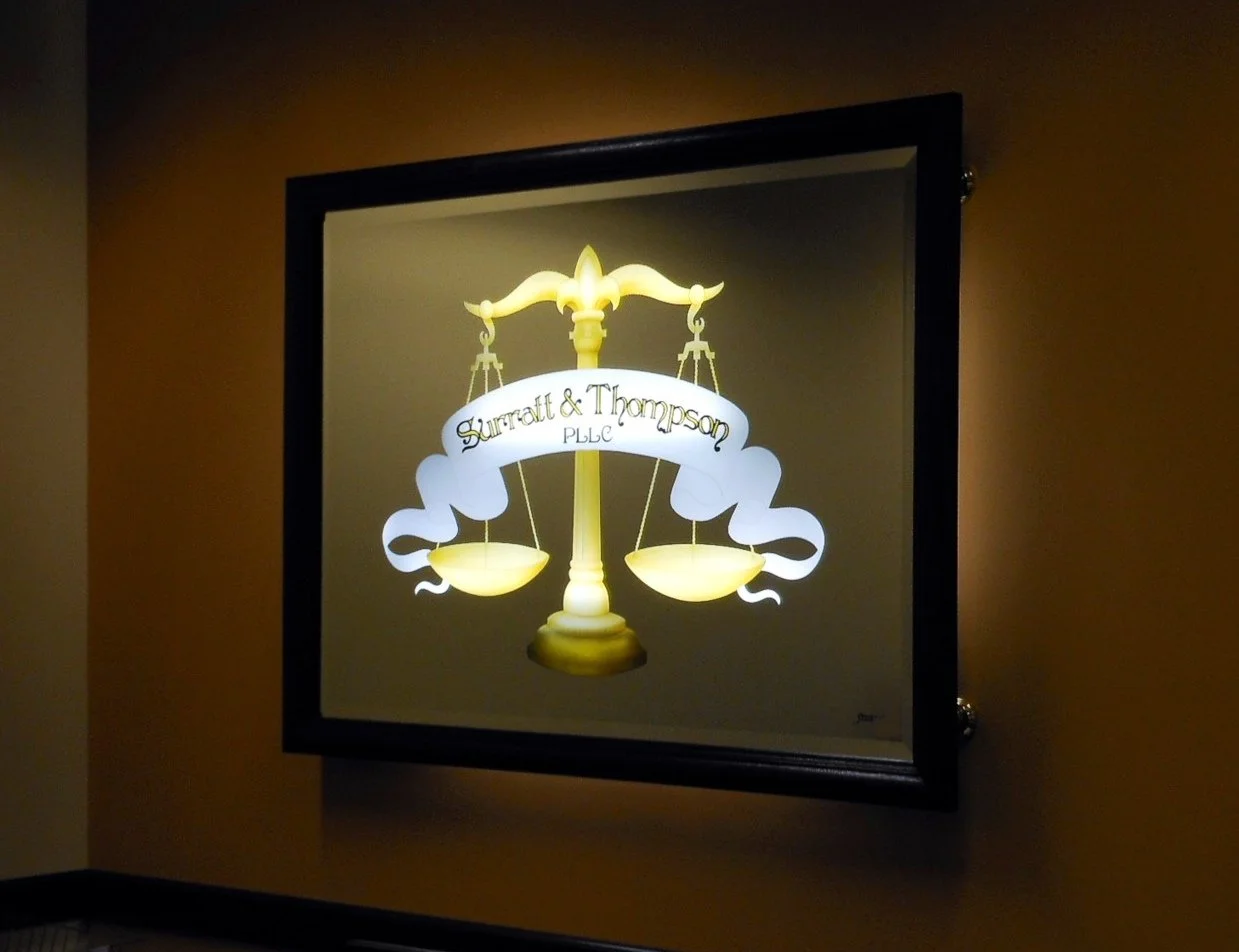 Illuminated mirror sign with scales of justice and a banner reading "Summitt & Thompson PLLC," wall mounted.
