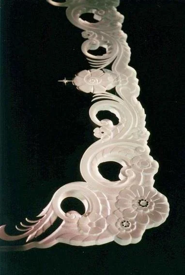 Sculpted and carved table edge with floral and swirling patterned design on a black background.