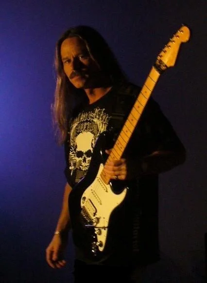 A person with long hair holding an electric guitar with a multicolored background