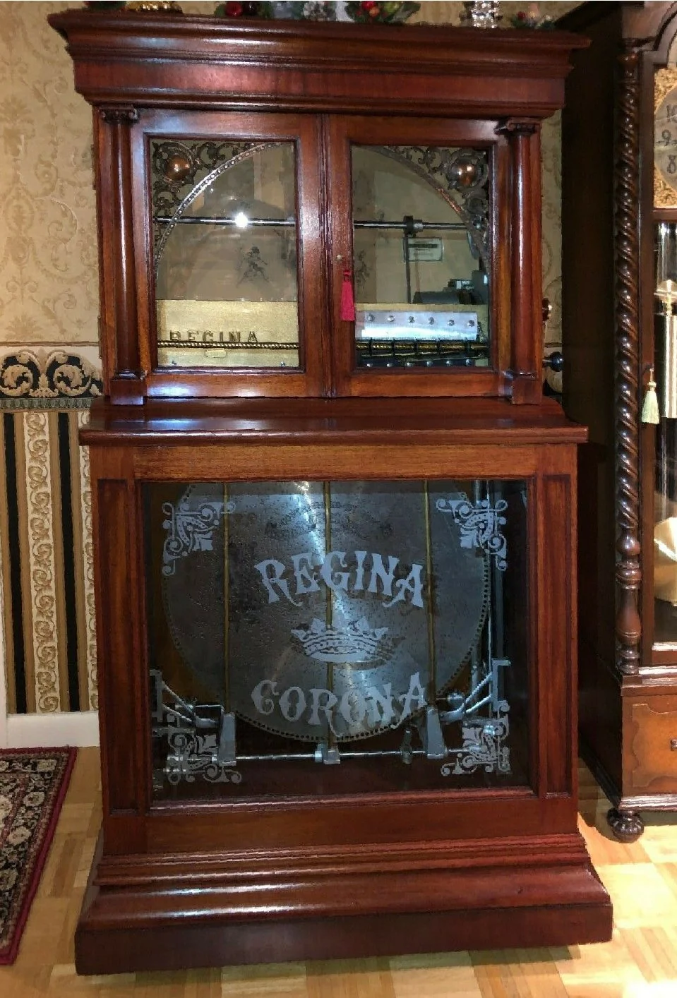 Vintage wooden furniture with etched glass doors, featuring the words 'REGINA CORONA' and decorative details, in a room with ornate wallpaper and a patterned rug.